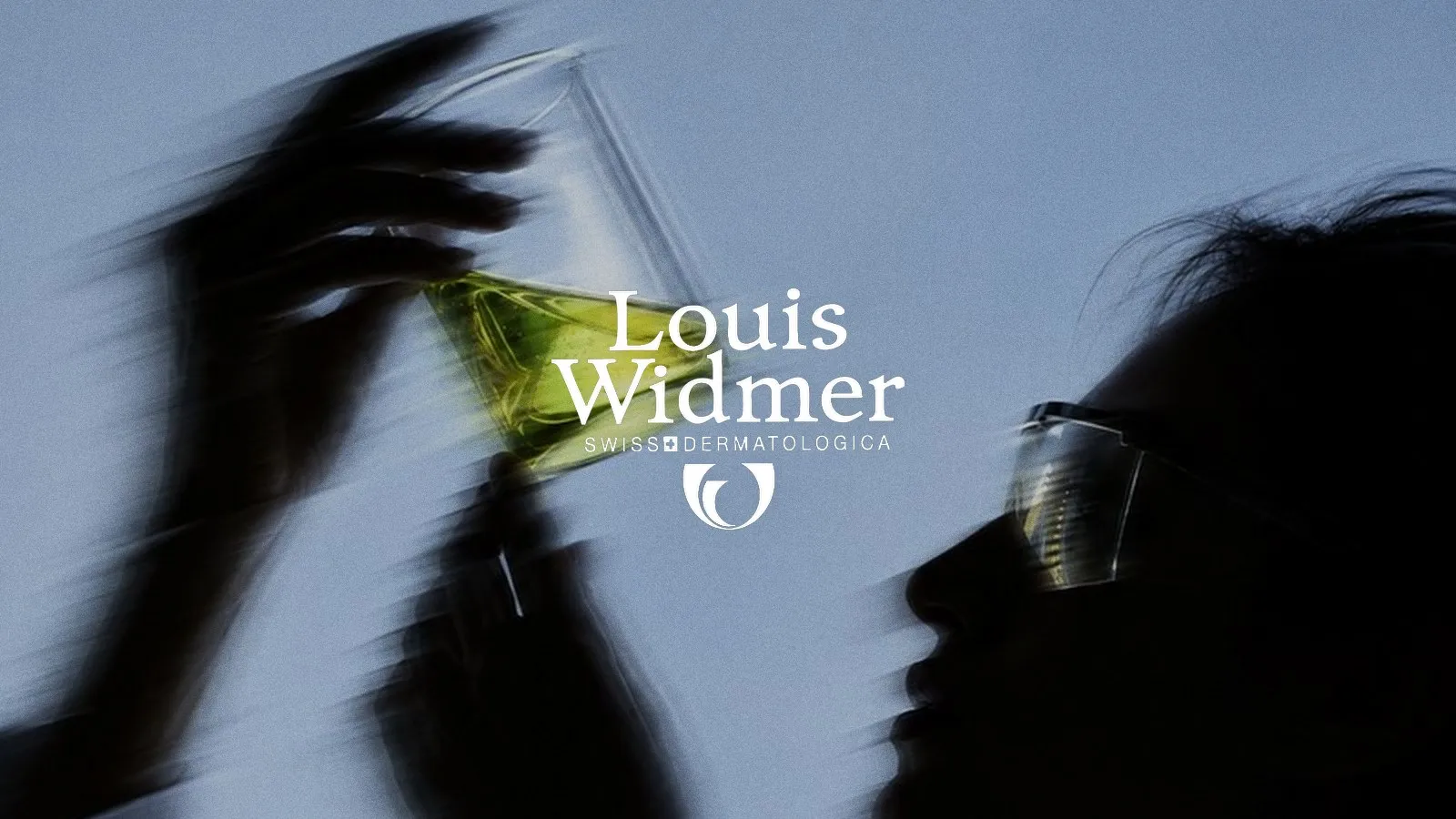 Eine Laborantin hält ein Becherglas mit grüner Flüssigkeit gegen das Licht, in der Mitte das weisse Logo von Louis Widmer
