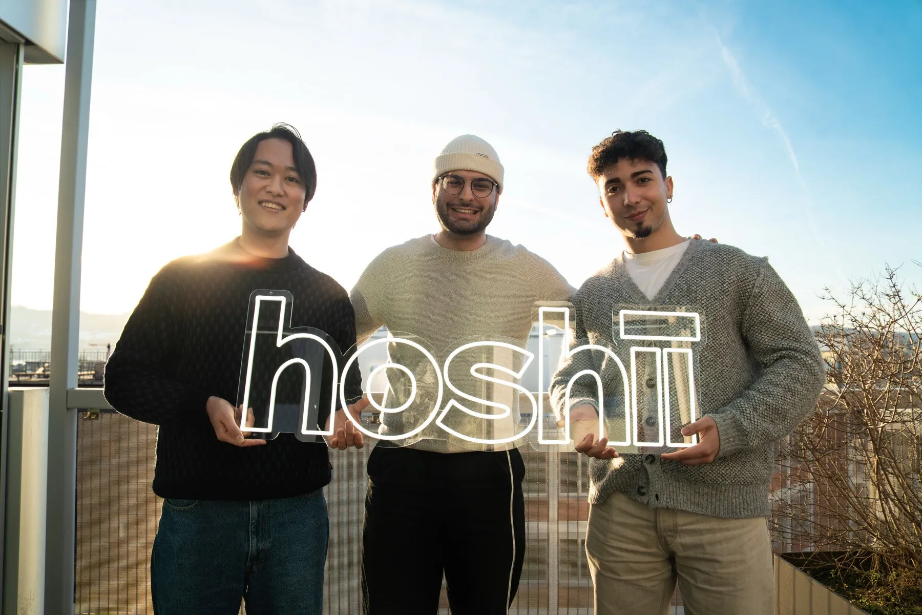 Die drei Hoshii‑Gründer auf einem Zürcher Dach, mit einem leuchtenden hoshii‑Schriftzug