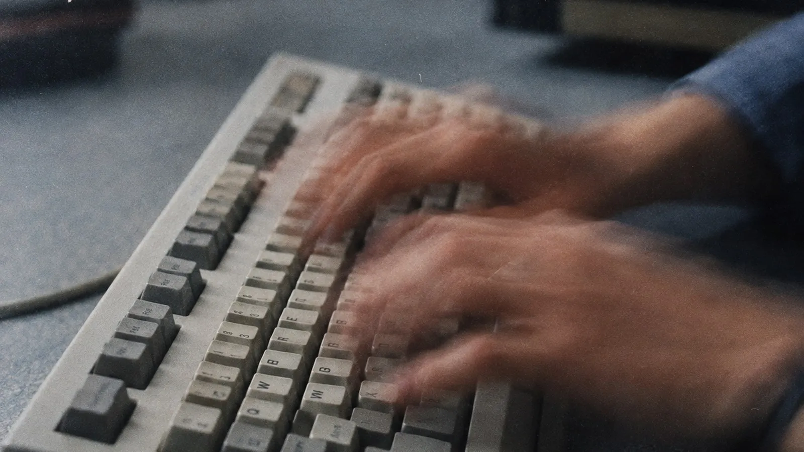 Zwei Hände tippen schnell auf einer alten Computertastatur.
