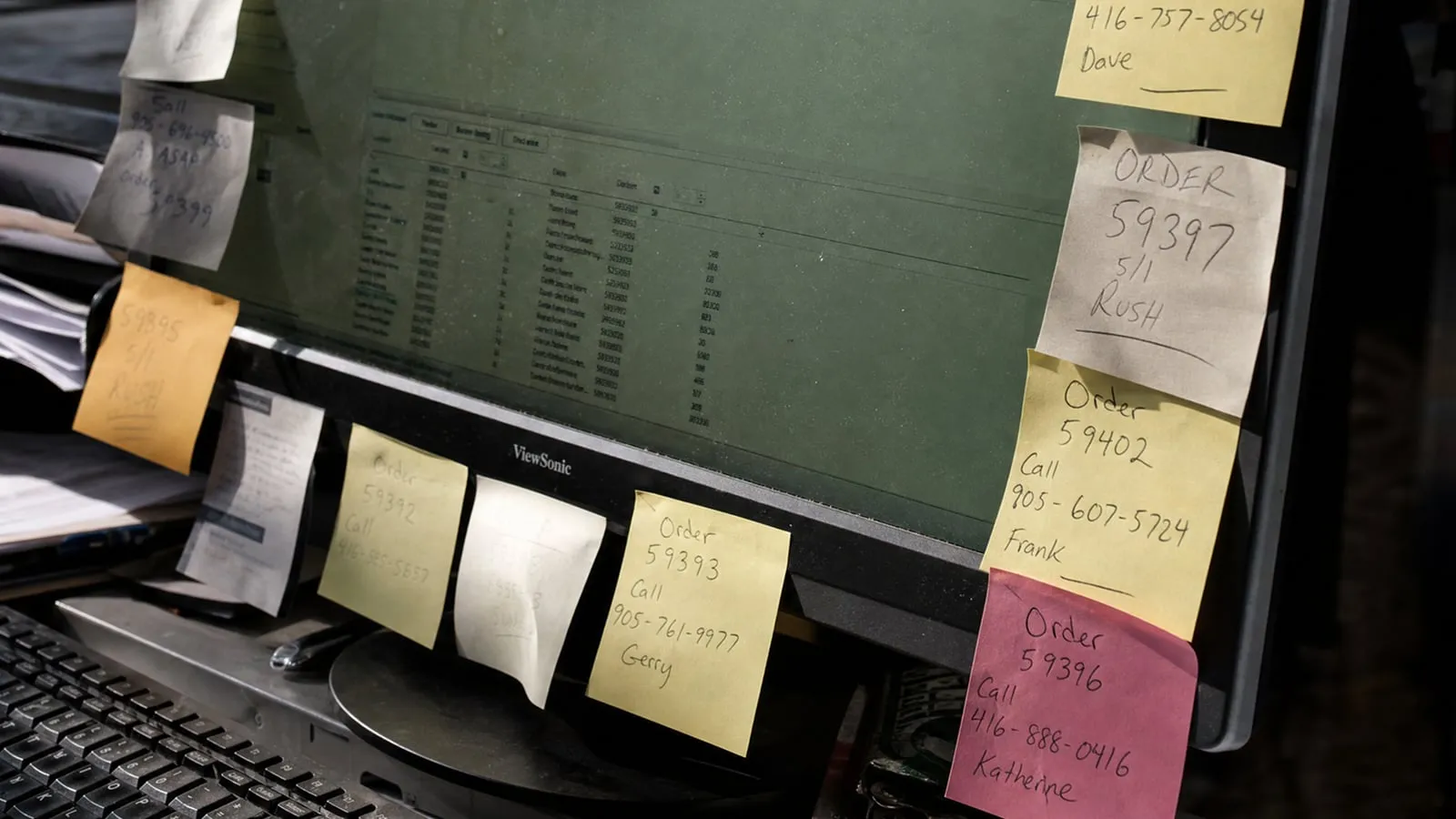 Ein Monitor voller Haftnotizen mit Bestellnummern und Telefonnummern.